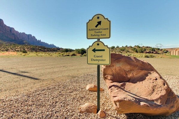 A signpost with directions to 'Additional Guest Trailer Parking Area' and 'Guest Dumpster' in a desert landscape. - Tranquil 2BR Mountainview Rim View with Hot Tub (Moab)