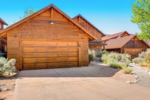 A wooden cabin with a garage, surrounded by desert vegetation. - Mountain View Home with Private Hot Tub & Patio - Close to Golf & Trails (Moab)