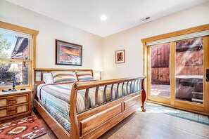 Een slaapkamer met een houten bed, een nachtkastje, een raam met uitzicht en een deur naar een buitenruimte.