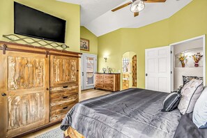 Een slaapkamer met een bed, een houten garderobe, een televisie en een plafondventilator.