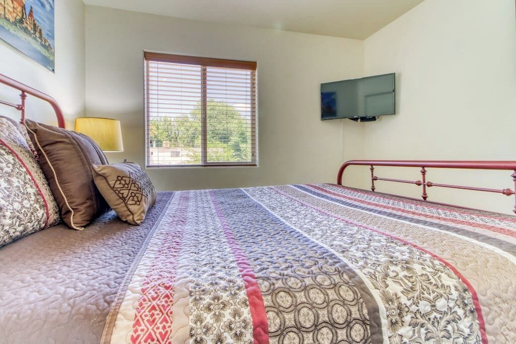 A bedroom with a bed, a window, and a television on the wall.