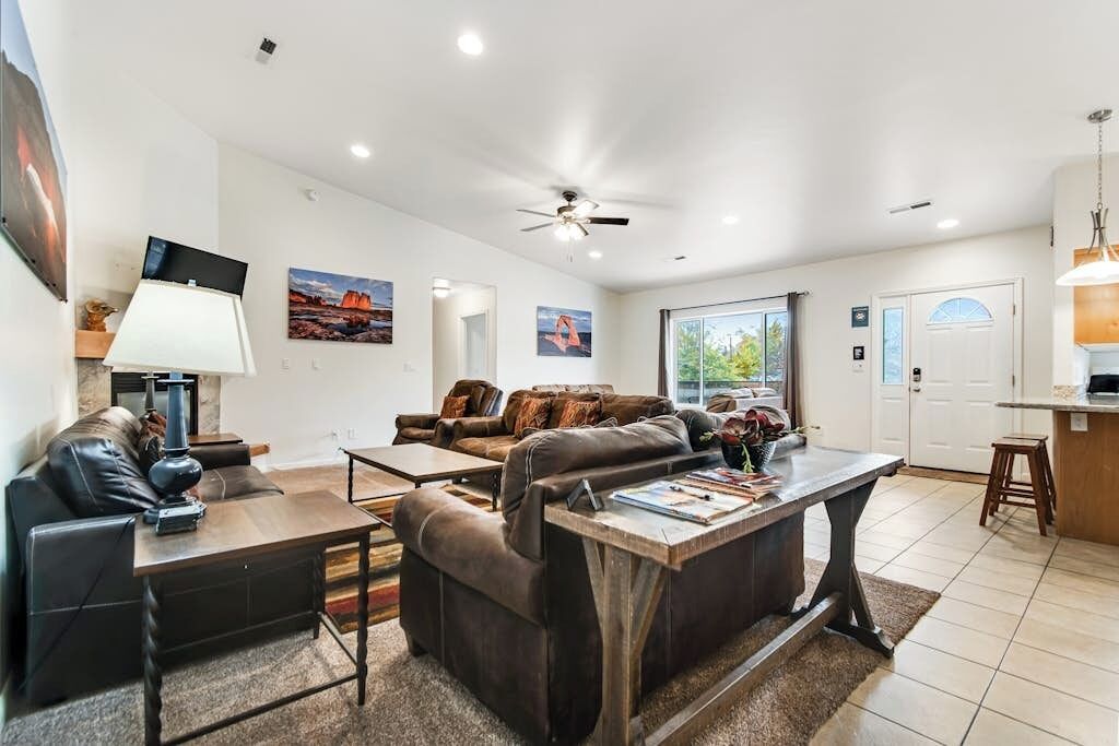 A spacious living room with a fireplace, a ceiling fan, and a large window.