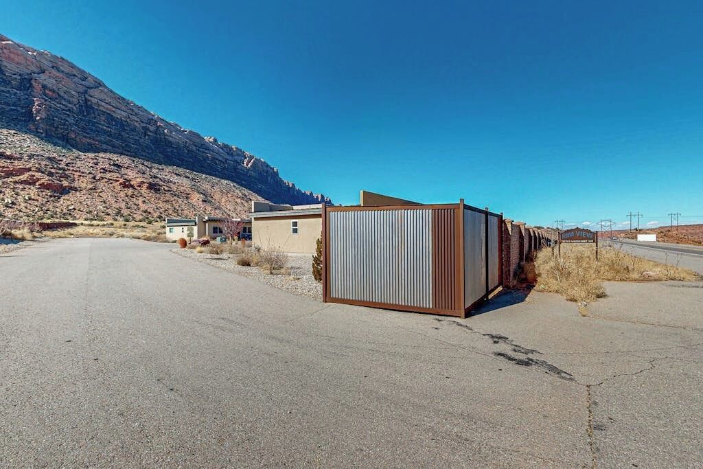 A rural road with a corrugated metal fence and a building with a flat roof.