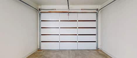 Un garaje con puerta blanca, estructura metálica y suelo de concreto.