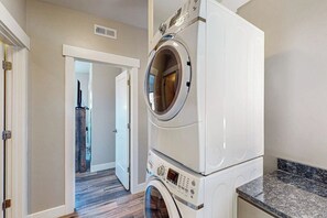 A laundry room with stacked washers and dryers, a door leading to another room, and a granite countertop. - 2 BR Rim View Moab Home with Mountain and Rock Views (Moab)