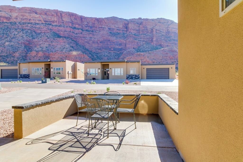 A building with a patio area featuring a table and chairs, set against a mountainous backdrop.