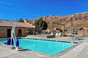 A swimming pool with a lifeguard stand, lounge chairs, and a mountain backdrop. - Townhome in Rim Village with Red Rock Views, Community Pool & Hot Tub (Moab)