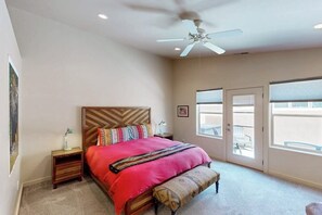 A bedroom with a bed, a bench, a nightstand, a ceiling fan, and a door leading to a balcony. - Townhome in Rim Village with Red Rock Views, Community Pool & Hot Tub (Moab)