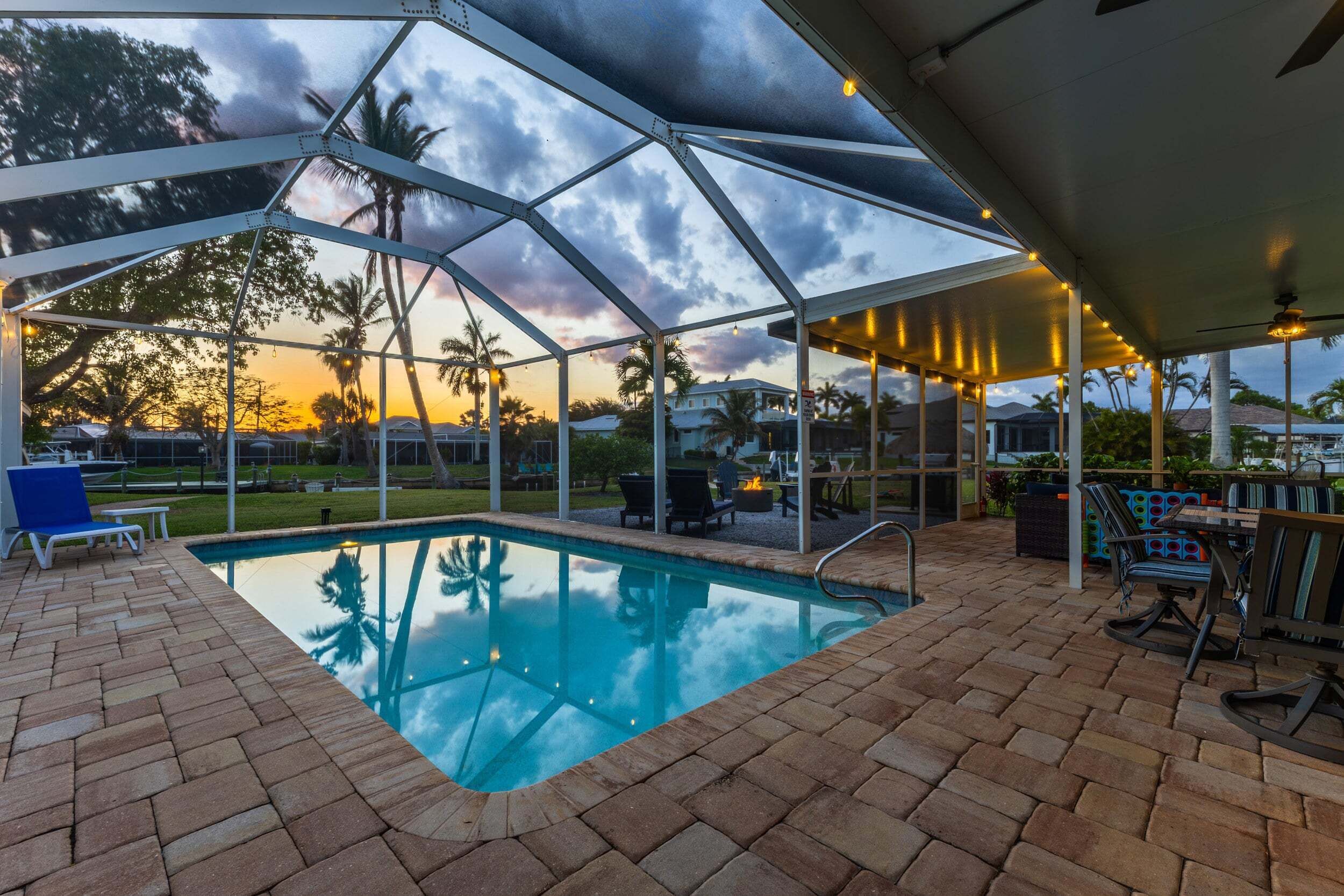 A covered outdoor pool area with a clear view of the sunset, lounge chairs, and a barbecue grill.