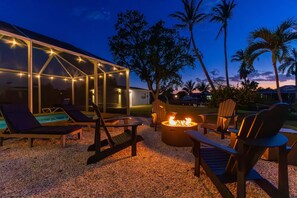 A glass-enclosed outdoor area with lounge chairs and a fire pit. - Gorgeous 4 BR, Pool Home, Game Room, Canal View, Sleeps 11! (Cape Coral)