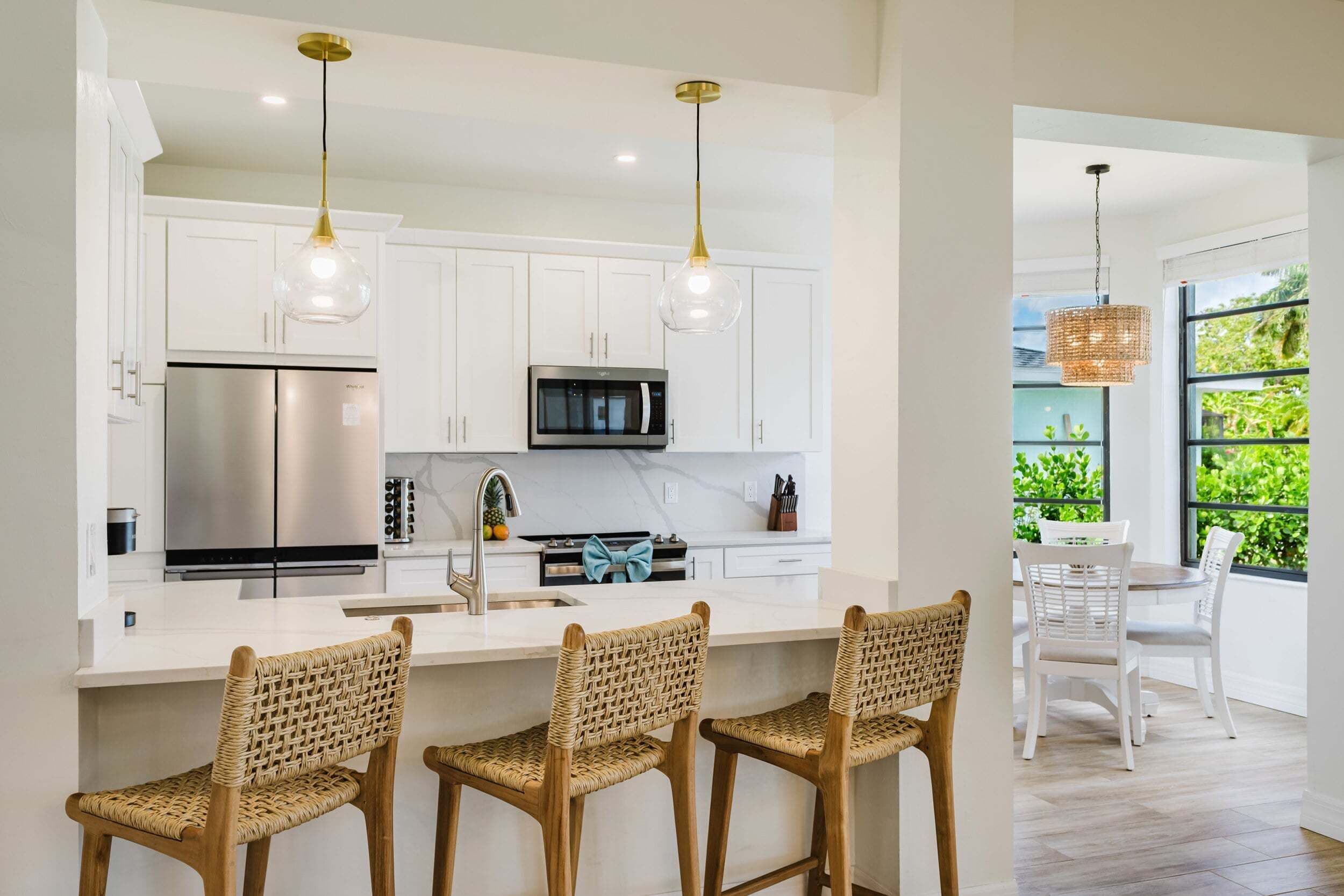 A modern kitchen with white cabinets, stainless steel appliances, and a bar area with wicker chairs.