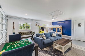 A room with a foosball table, a sofa, a coffee table, and a bunk bed. - Gorgeous 4 BR, Pool Home, Game Room, Canal View, Sleeps 11! (Cape Coral)