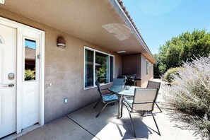 A residential building with a patio area featuring a table and chairs, a sliding door, and a small outdoor kitchen. - Dog-Friendly Townhome with WiFi, Nice Views & Indoor Pool (Moab)