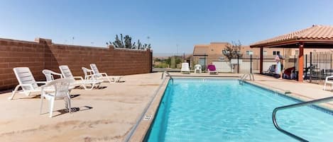 Une piscine bordée de chaises longues blanches et d’un mur en briques.