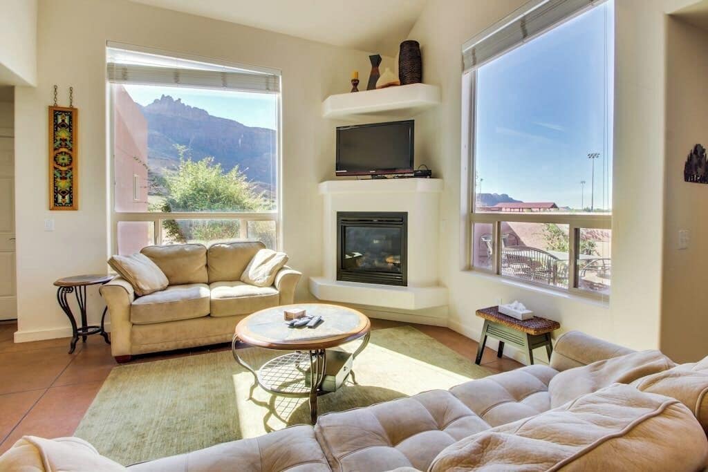 A living room with a sofa, a coffee table, a fireplace, and large windows offering a mountain view.