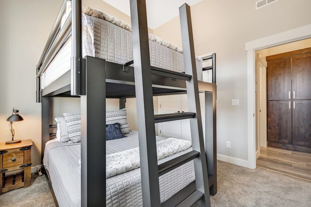 Una cama litera con escalera de madera, una mesita de noche con lámpara y un armario al fondo.