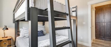 Una cama litera con escalera de madera, una mesita de noche con lámpara y un armario al fondo.