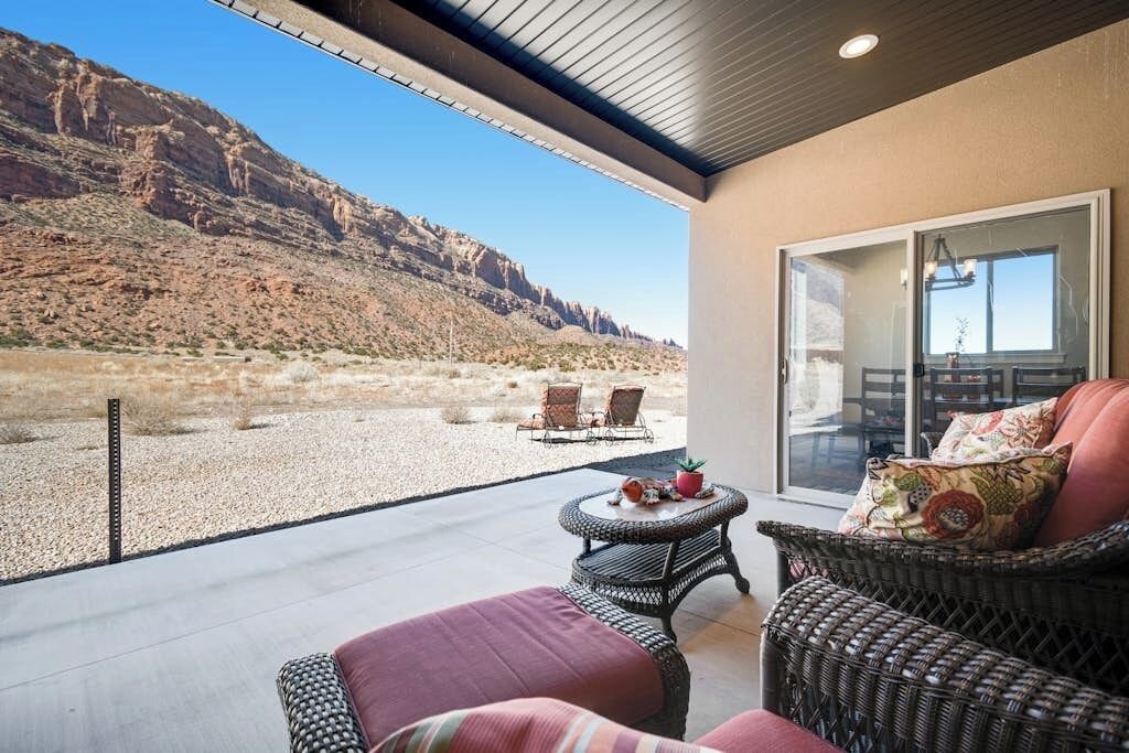Un balcon doté de meubles en osier, une vue sur un paysage désertique et une porte vitrée donnant sur un espace intérieur.
