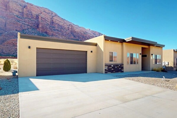 Ein modernes, zweistöckiges Haus mit Garage, Auffahrt und Blick auf die Berge.