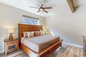 Ein Schlafzimmer mit einem hölzernen Bett, Nachttischen, einem Deckenventilator und einem Fenster mit Ausblick.