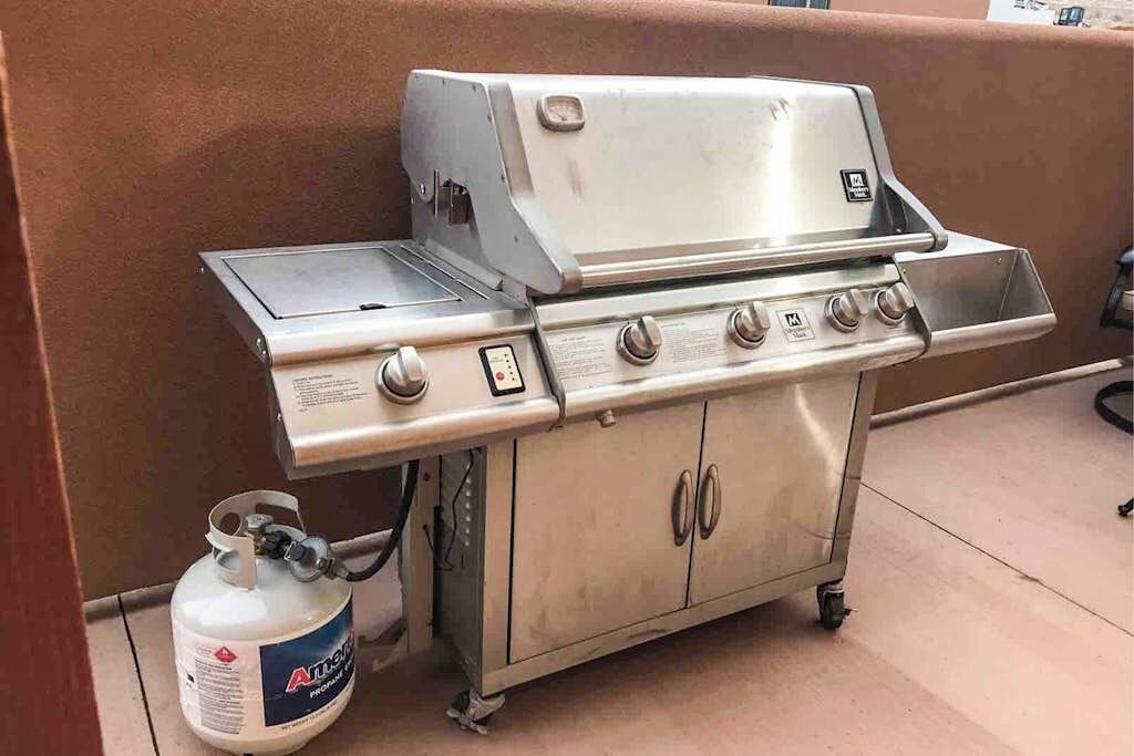 Ein tragbarer Grill aus Edelstahl mit Seitenbrenner und Propangasflasche.