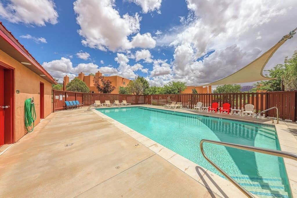 A swimming pool with lounge chairs, a fence, and a clear sky.