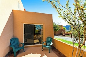 A patio with two chairs, a sliding glass door, and a view of a landscaped area. - Lovely Moab Townhouse with Shared Pool Near Arches National Park (Moab)