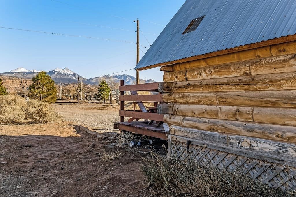 A rustic wooden cabin with a metal roof, situated in a mountainous area with sparse vegetation.