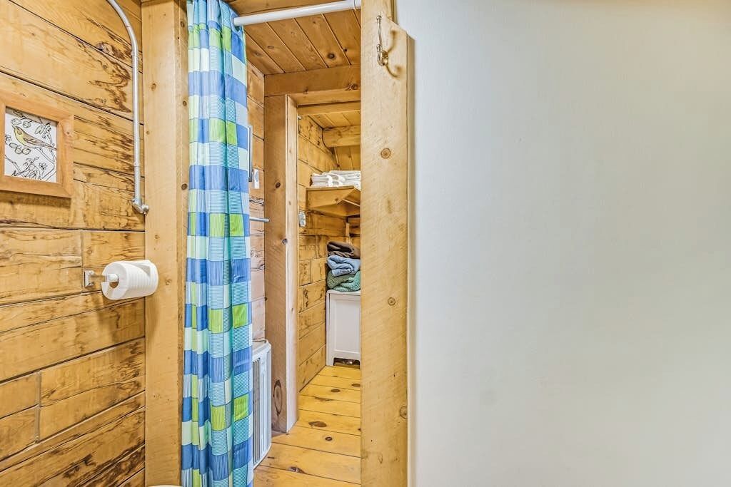 A wooden interior with a shower curtain, a toilet, and a storage area with shelves.