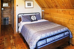 Une chambre avec un lit en métal, une literie à motifs, des murs en bois et un plafond en pente.