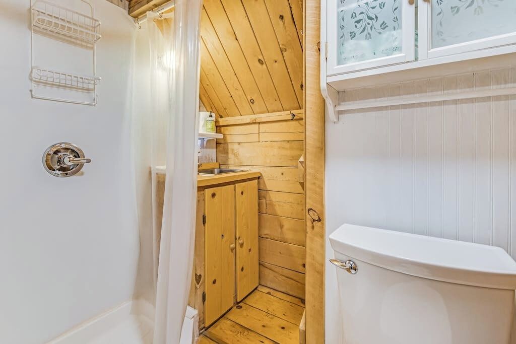 Un baño pequeño con piso de madera, un inodoro blanco y un armario de madera.