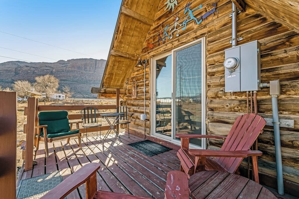 A wooden cabin with a deck, a large sliding glass door, and a view of the mountains.