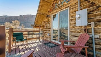 A wooden cabin with a deck, a large sliding glass door, and a view of the mountains.