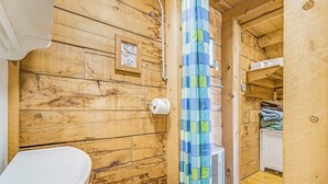 Un interior de madera con un inodoro, cortina de ducha y un pequeño estante con toallas dobladas.