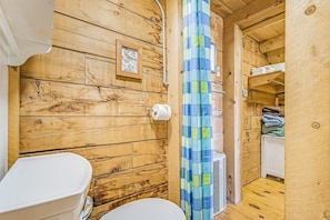 Un interior de madera con un inodoro, cortina de ducha y un pequeño estante con toallas dobladas.