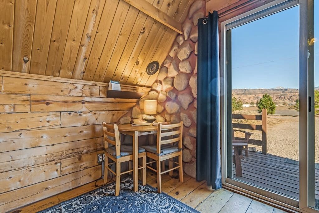 Een houten interieur met een stenen muur, een ronde tafel met stoelen en een uitzicht door een glazen deur.