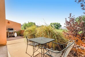 An outdoor patio with a metal table and chairs, a barbecue grill, and a view of a grassy field. - Redesigned Red Rock Condo with Golf Course View, Patio, Fireplace, AC & Pool (Moab)