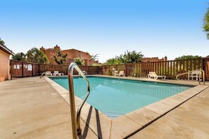 A swimming pool with a metal ladder, surrounded by a wooden fence, and white lounge chairs. - Redesigned Red Rock Condo with Golf Course View, Patio, Fireplace, AC & Pool (Moab)