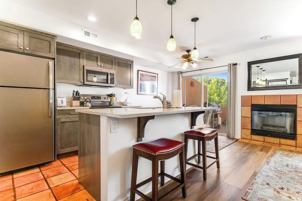 A kitchen with a central island, bar stools, a microwave, and a fireplace.