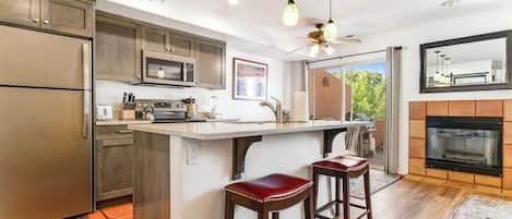 A kitchen with a central island, bar stools, a microwave, and a fireplace.