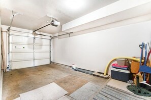 Een garage met een witte garagedeur, een projector aan het plafond en verschillende schoonmaakmiddelen op de vloer.