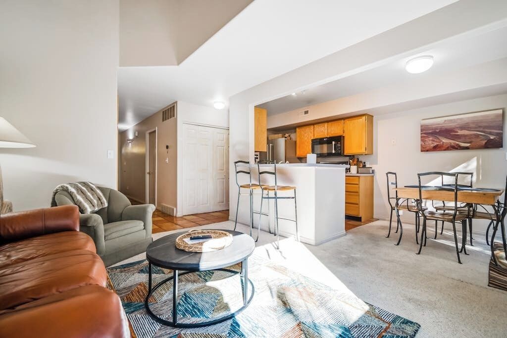 Un espace de vie moderne comprenant un canapé, une table basse et une table à manger avec des chaises. Il y a également un coin cuisine avec des placards et un réfrigérateur.