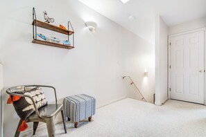 Una habitación con una puerta blanca, un radiador, una silla con cojín estampado y un estante con adornos.