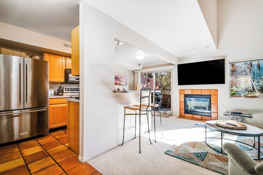 A modern kitchen with a stainless steel refrigerator, wooden cabinets, and a dining area with a fireplace.