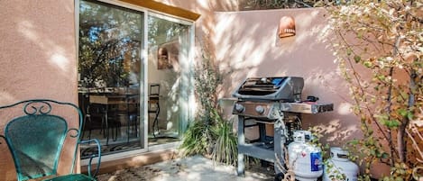 A patio with a grill, a chair, and a glass door leading to a room.