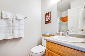 Ein Badezimmer mit Toilette, Waschbecken und Spiegel. Handtücher hängen an der Wand.
