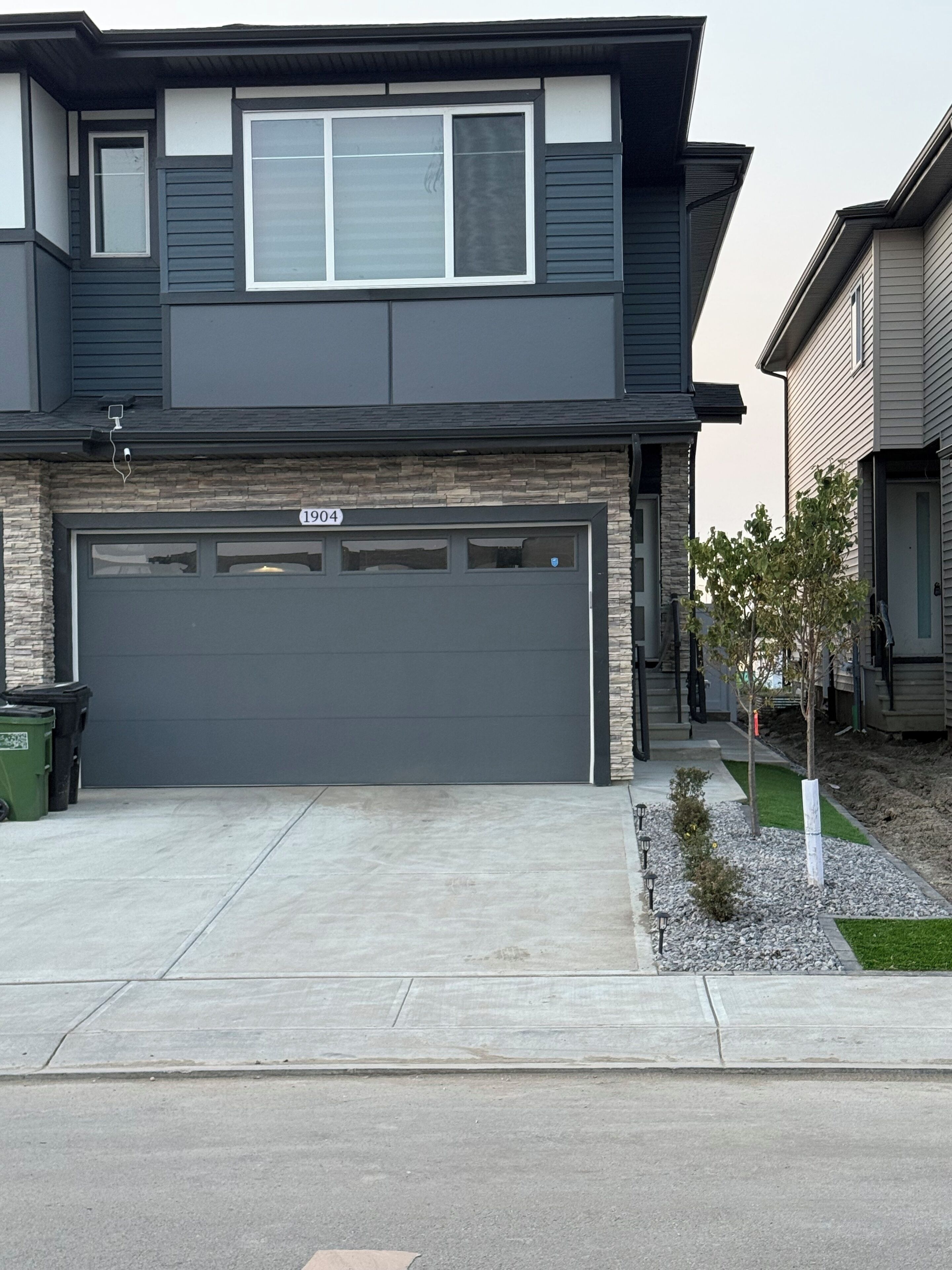 A two-story house with a garage, stone facade, and a small front yard with a tree.