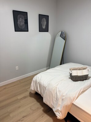 Ein Schlafzimmer mit einem Bett, einem Nachttisch, einem Spiegel und zwei gerahmten Kunstwerken an der Wand.