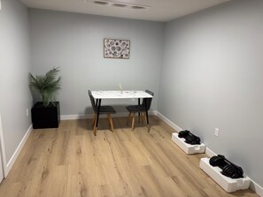 Een eethoek met een tafel, stoelen, een potplant en een kunstwerk aan de muur.