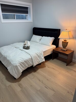 Een slaapkamer met een bed, nachtkastje, lamp, raam en een wandplank.